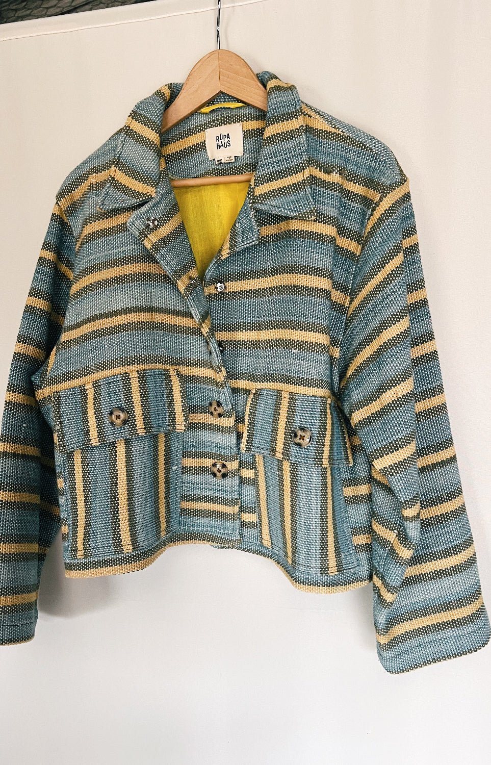 A striped multicolored jacket with asymmetrical deep pocket placement and button detailing, hanging on a hanger against a white background.