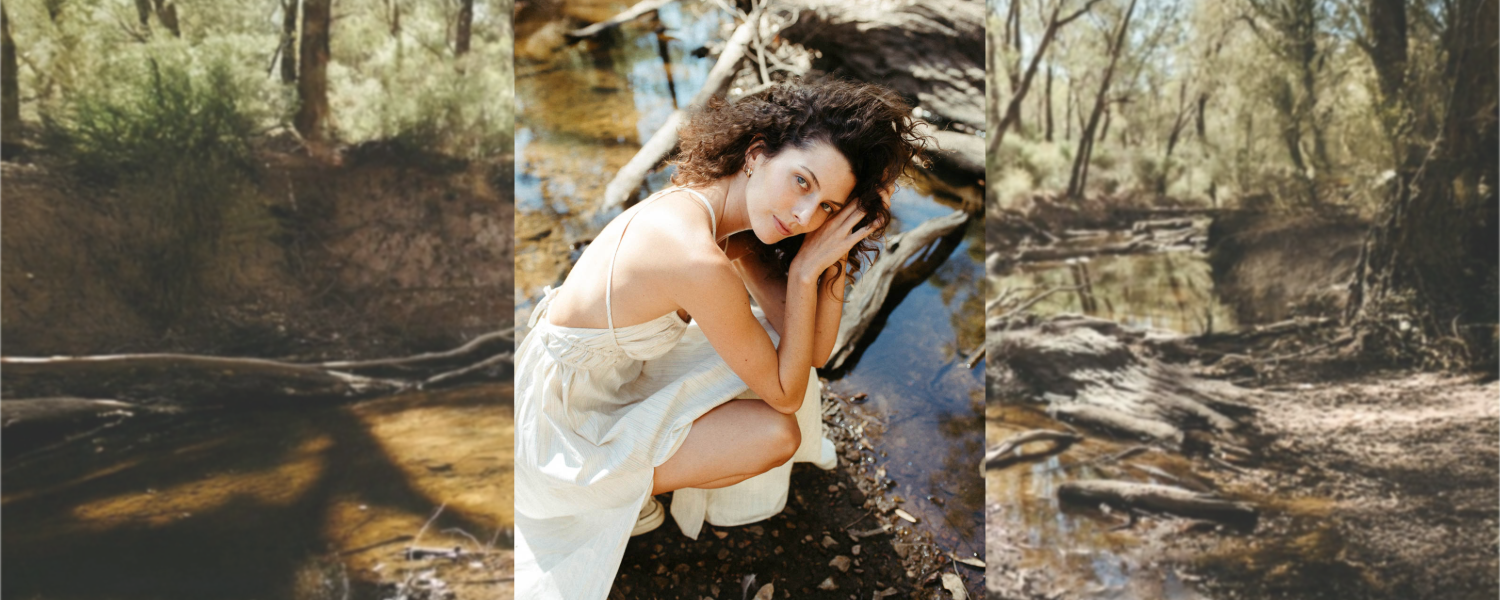 Model wearing RŪPAHAUS handcrafted dress beside a forest creek, reflecting slow fashion, natural materials, and artisan-made clothing