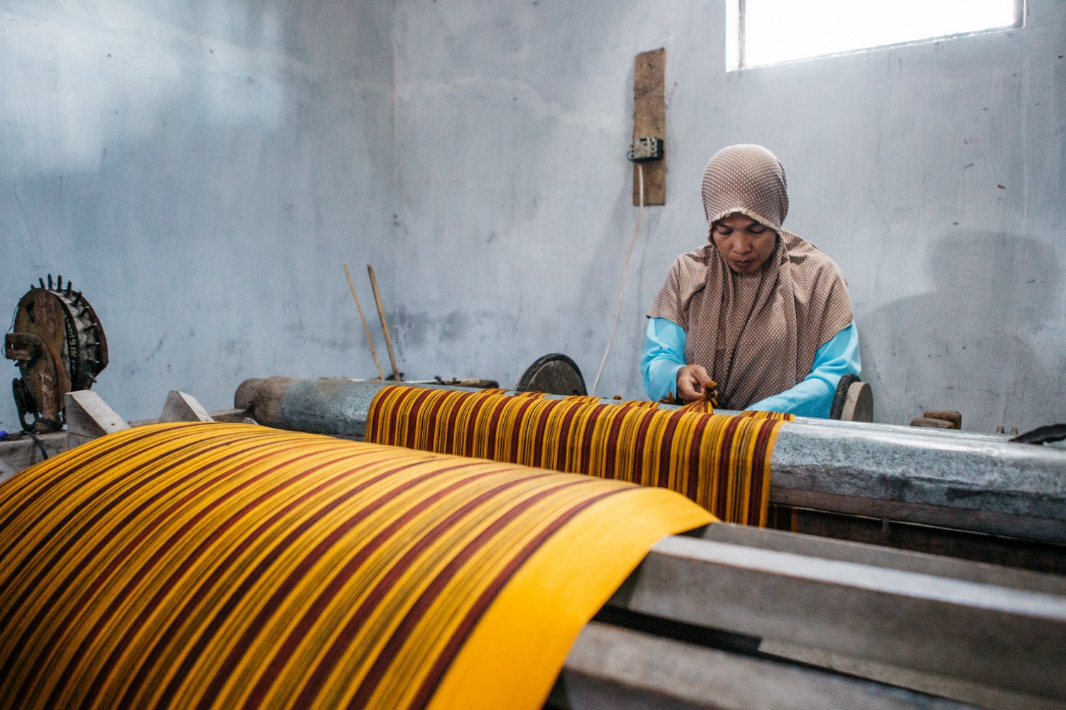 Artisan working at a traditional loom in Indonesia, weaving striped fabric as part of a long-term, small-batch textile collaboration.