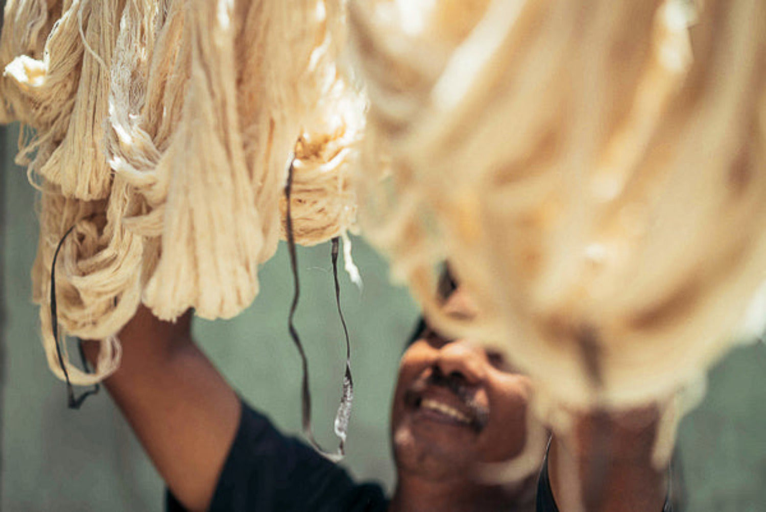 Artisan lifting hand-prepared cotton yarn during textile making, reflecting long-term partnership, shared process, and living craft traditions in Indonesia.