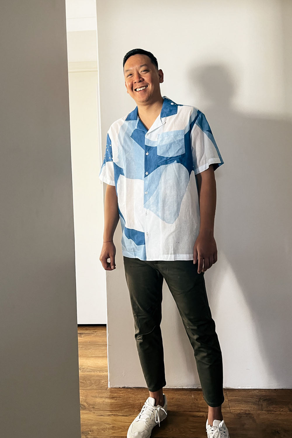A handpainted batik cotton shirt with a relaxed collar, featuring indigo and natural hues with contrasting color buttons and a chest pocket, worn by a male model.