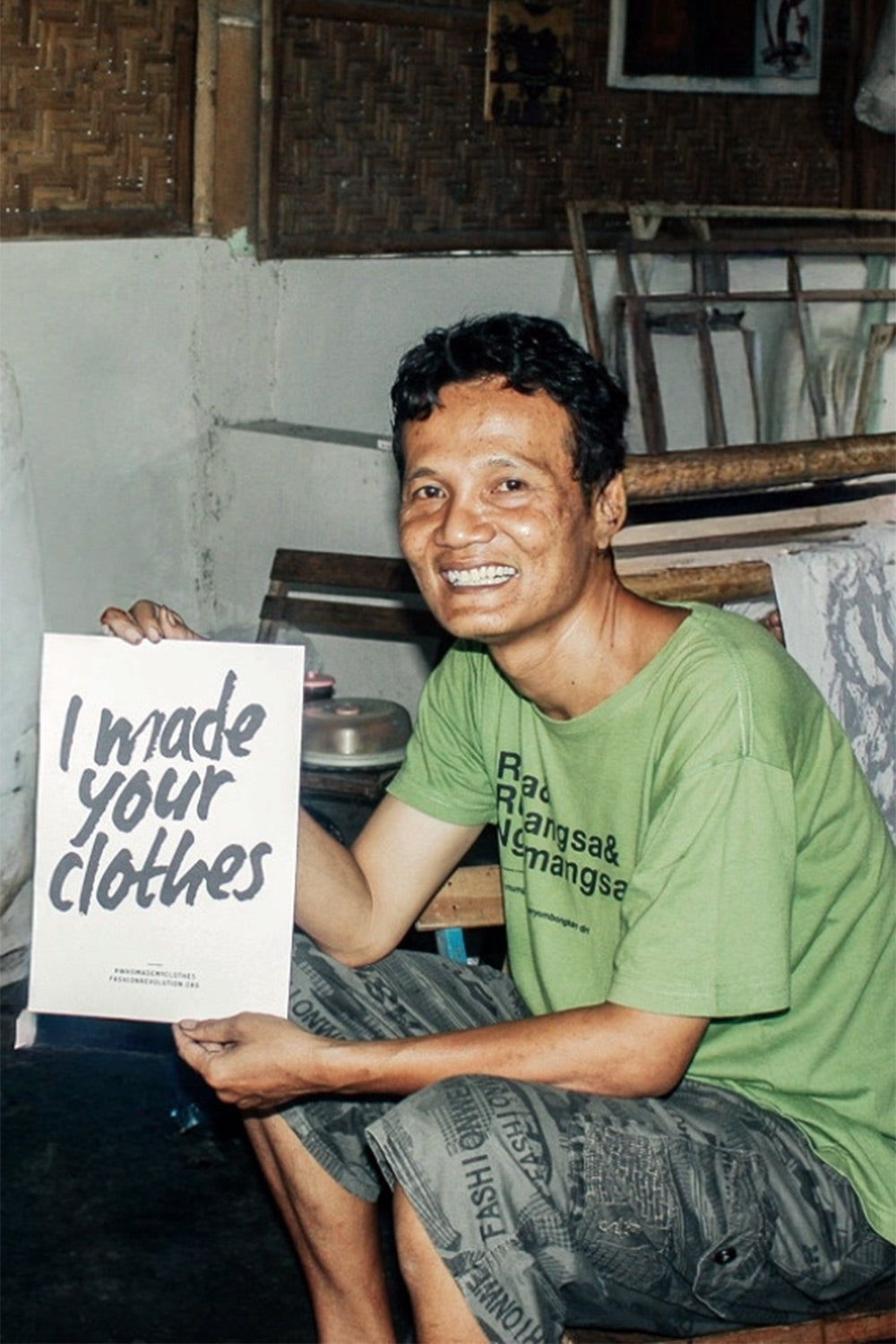 Batik Master holding an “I made your clothes” sign inside a textile workshop setting
