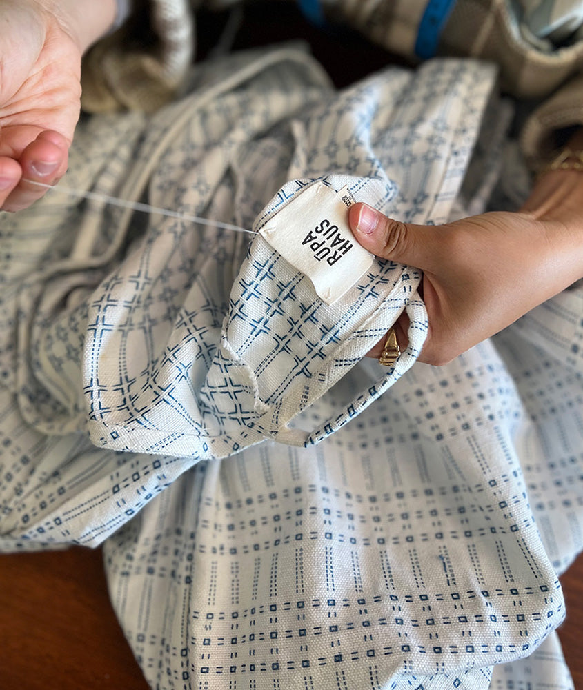Hands sewing a RŪPAHAUS label onto a garment during the finishing process, reflecting small-batch, thoughtful production.
