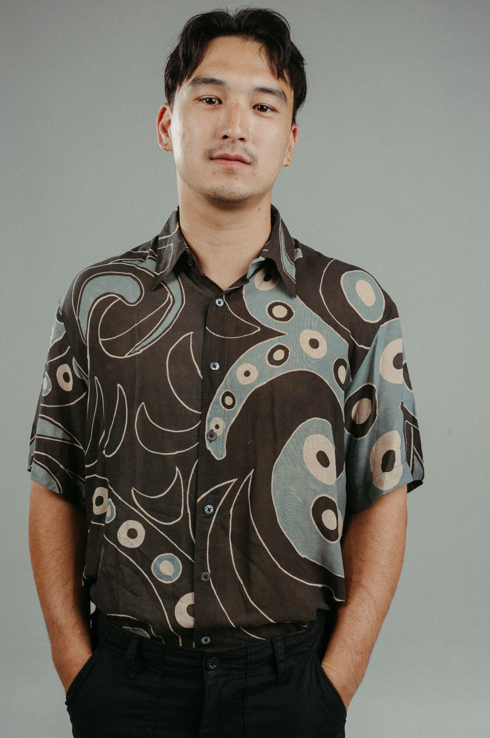 A person wearing a brown handpainted batik shirt with a geometric pattern featuring circles and lines.