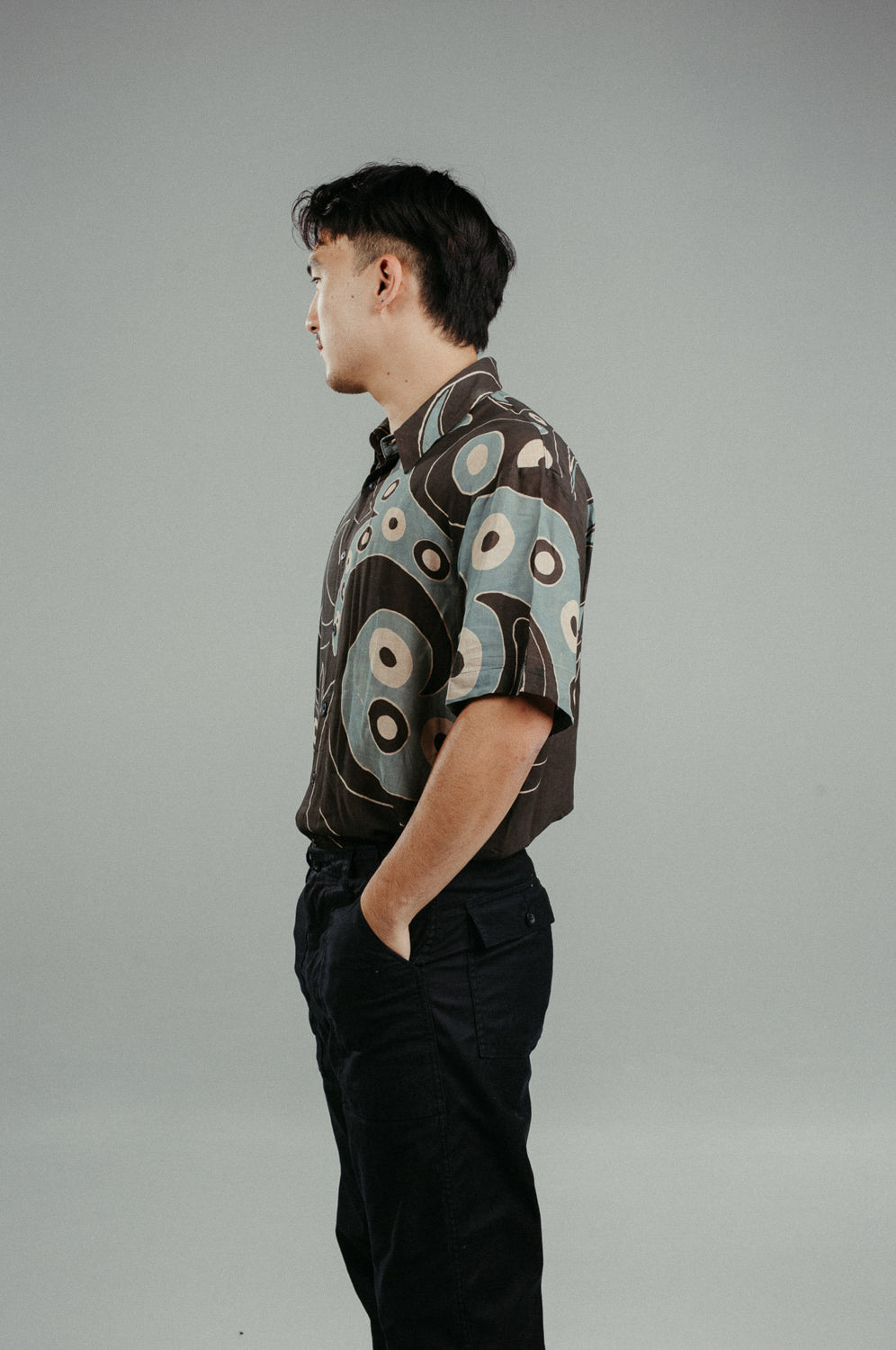 A person wearing a brown handpainted batik shirt with a geometric pattern featuring circles and lines.