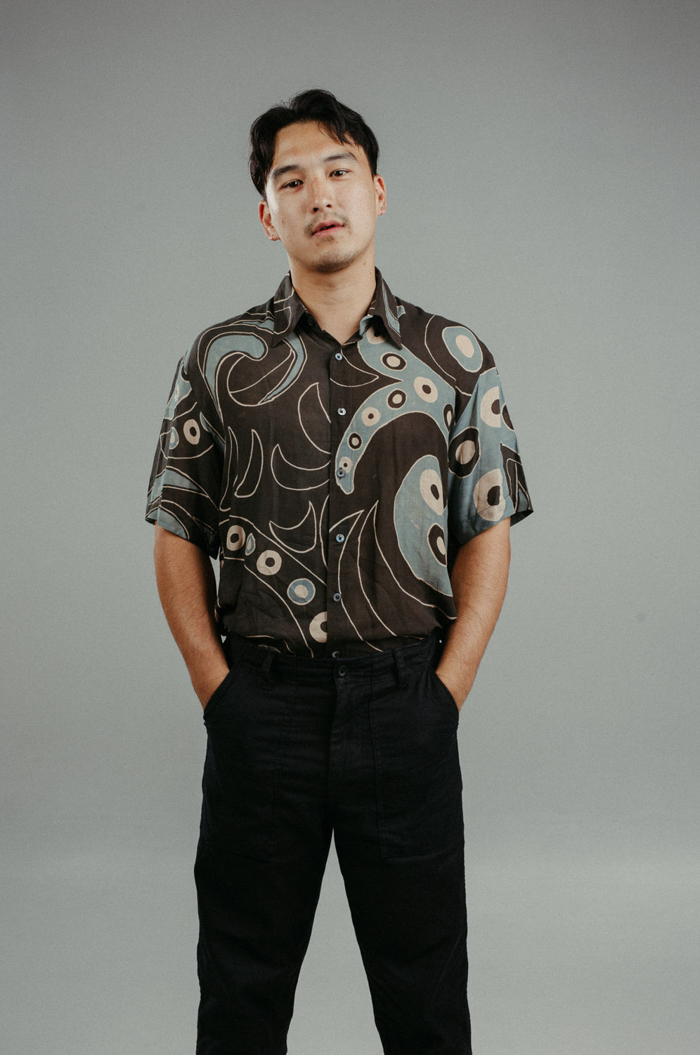 A person wearing a brown handpainted batik shirt with a geometric pattern featuring circles and lines.