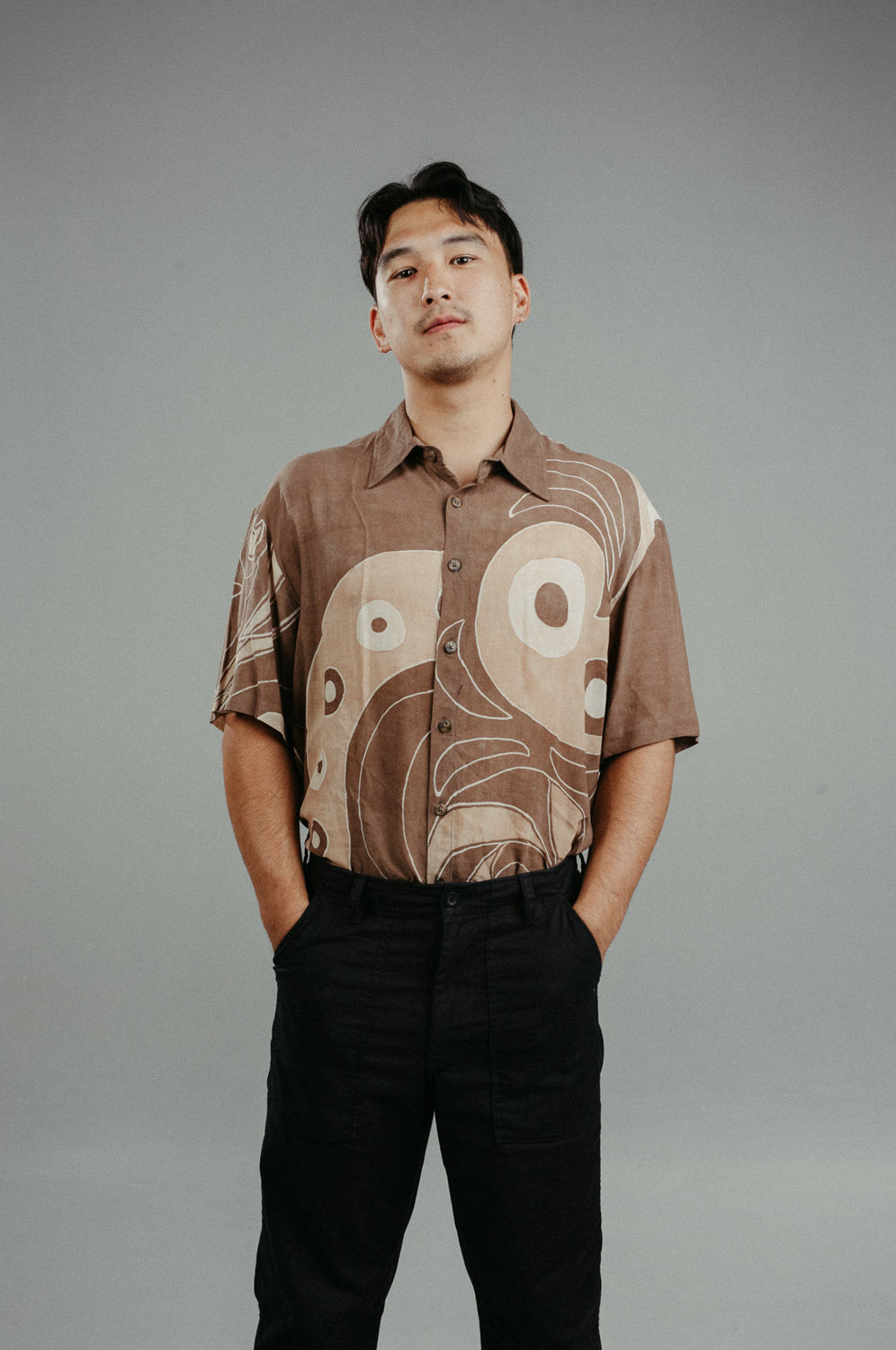 A person wearing a brown handpainted batik shirt with geometric patterns and a classic collar, featuring contrasting recycled seashell marble buttons.
