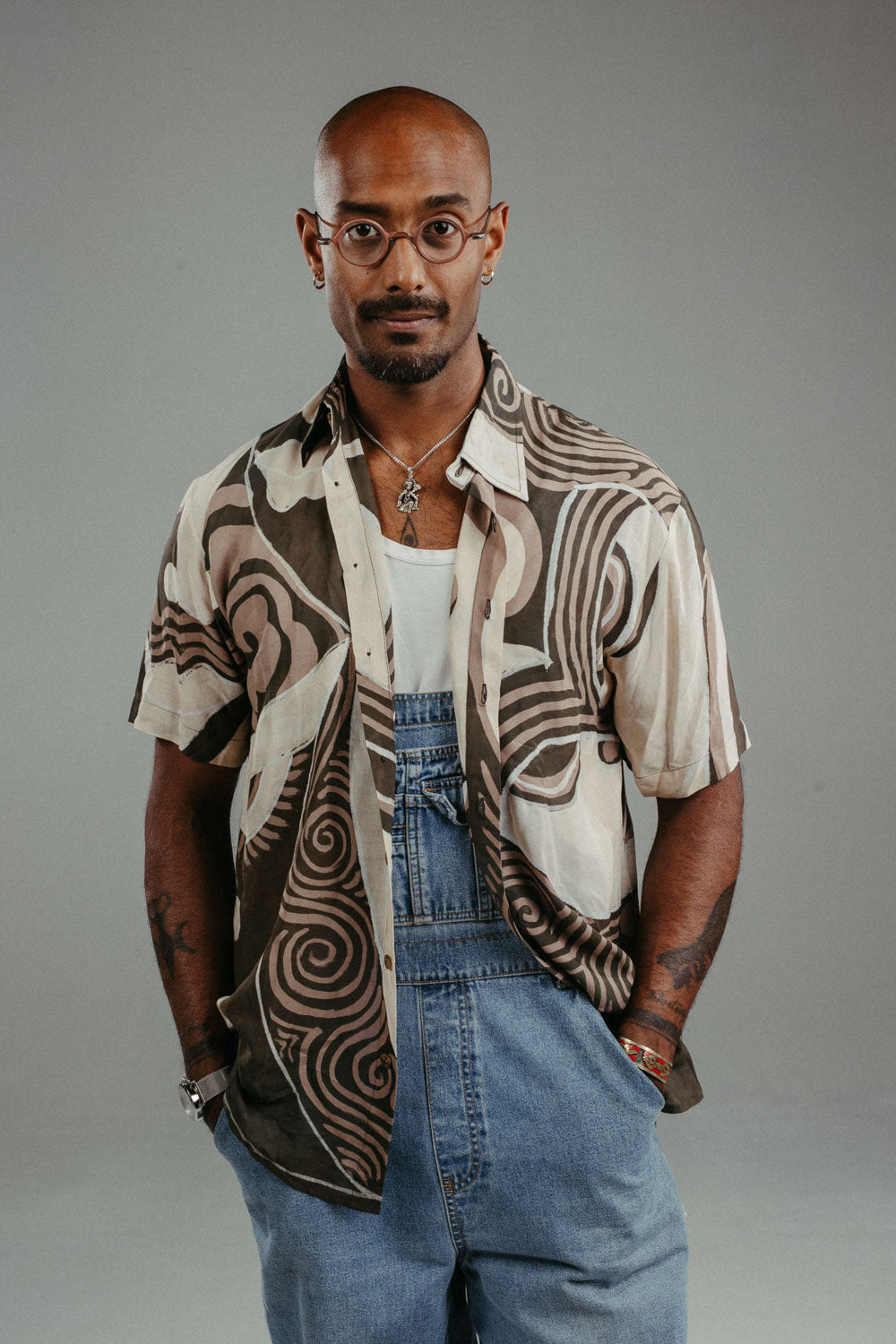 Handpainted Batik cotton shirt worn by a male model in a brown and natural hues featuring pattern of wayang faces.