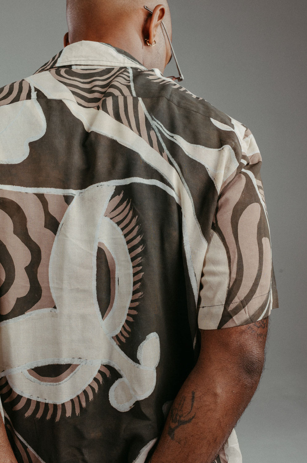 Handpainted Batik cotton shirt worn by a male model in a brown and natural hues featuring pattern of wayang faces.