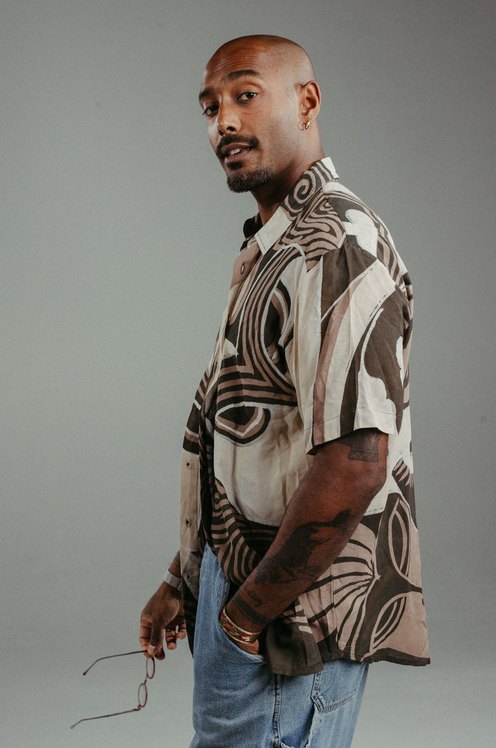 Handpainted Batik cotton shirt worn by a male model in a brown and natural hues featuring pattern of wayang faces.