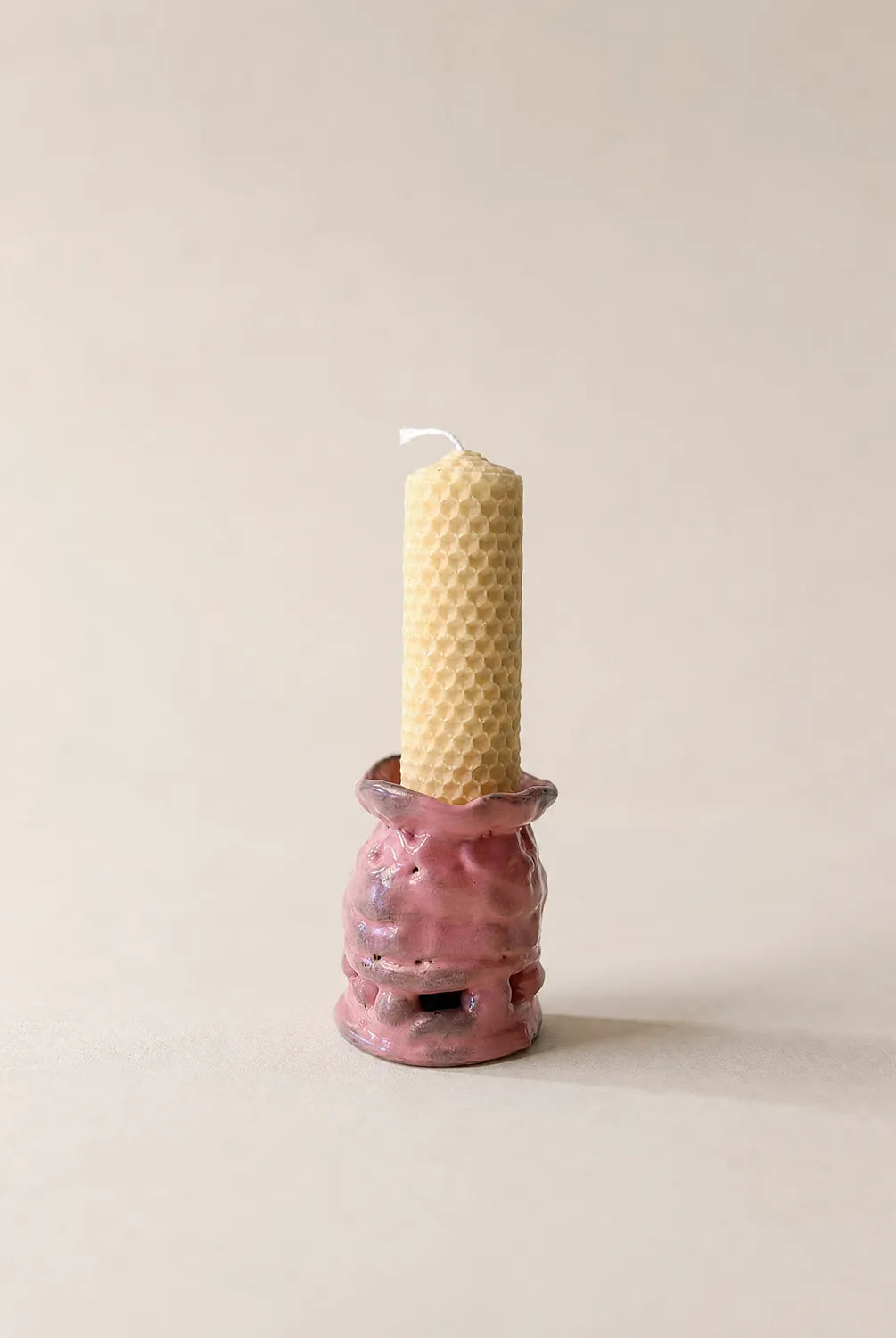 Pink ceramic candle holder with a textured surface holding a beeswax candle on a beige background