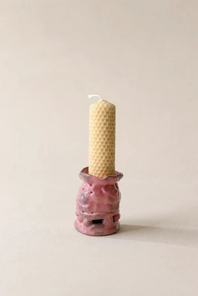 Pink ceramic candle holder with a textured surface holding a beeswax candle on a beige background
