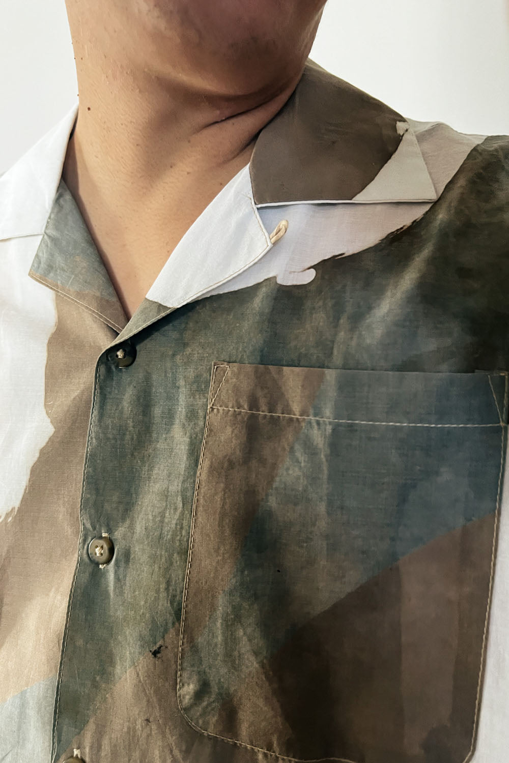upclose image of a handpainted batik cotton shirt in beige, brown, and white colors, worn by a male model