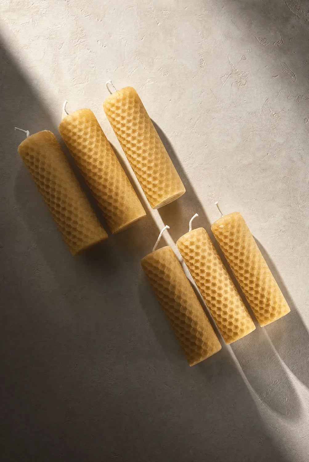 Three honeycomb-patterned beeswax candles on a textured surface
