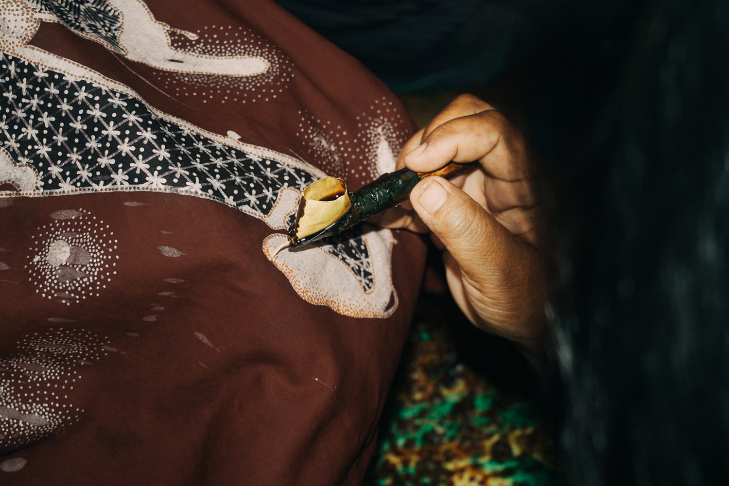 Close-up of rupahaus artisan applying hot wax with a canting tool to hand-drawn batik fabric during the dye-resist process