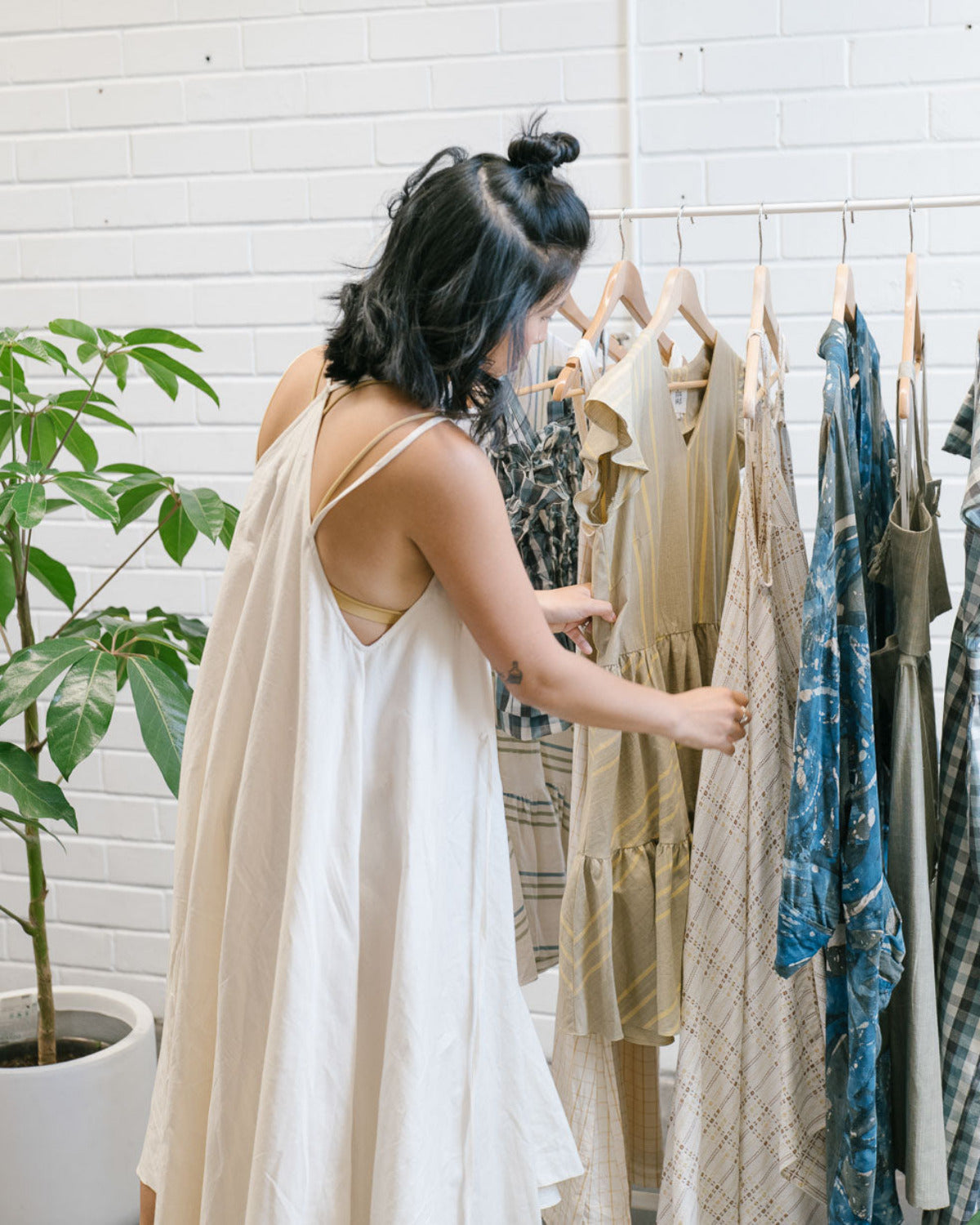 A woman selecting natural fibre garments from a cohesive RŪPAHAUS clothing rack, illustrating how to build a seasonless wardrobe through adaptable silhouettes and repeatable pieces.