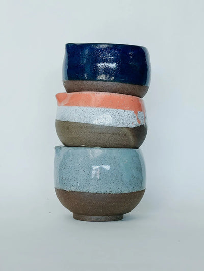 Stack of three ceramic cups with different color patterns on a light gray background