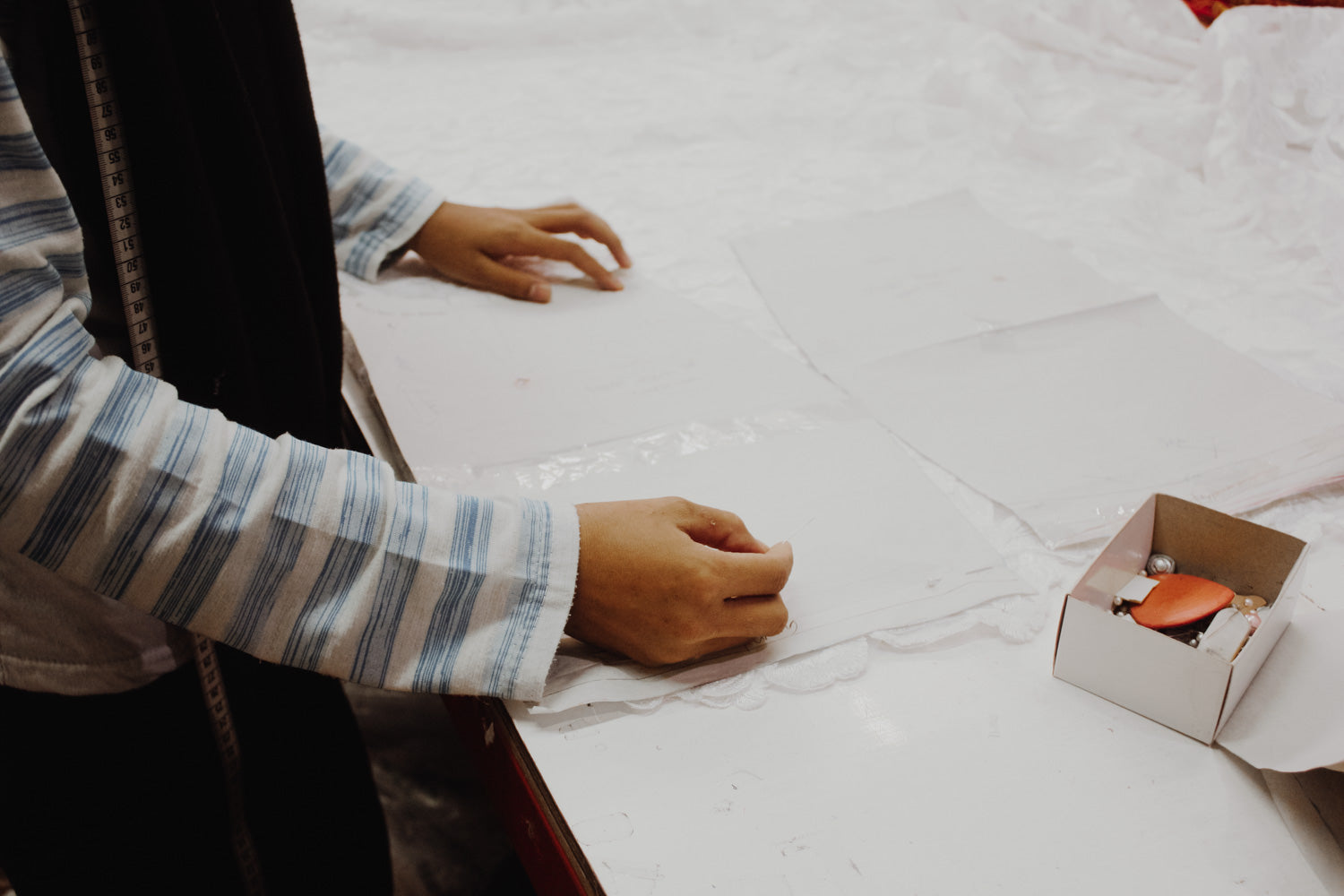 Hands adjusting garment pattern pieces during small-batch production, reflecting careful, human-led garment making in Indonesia. 