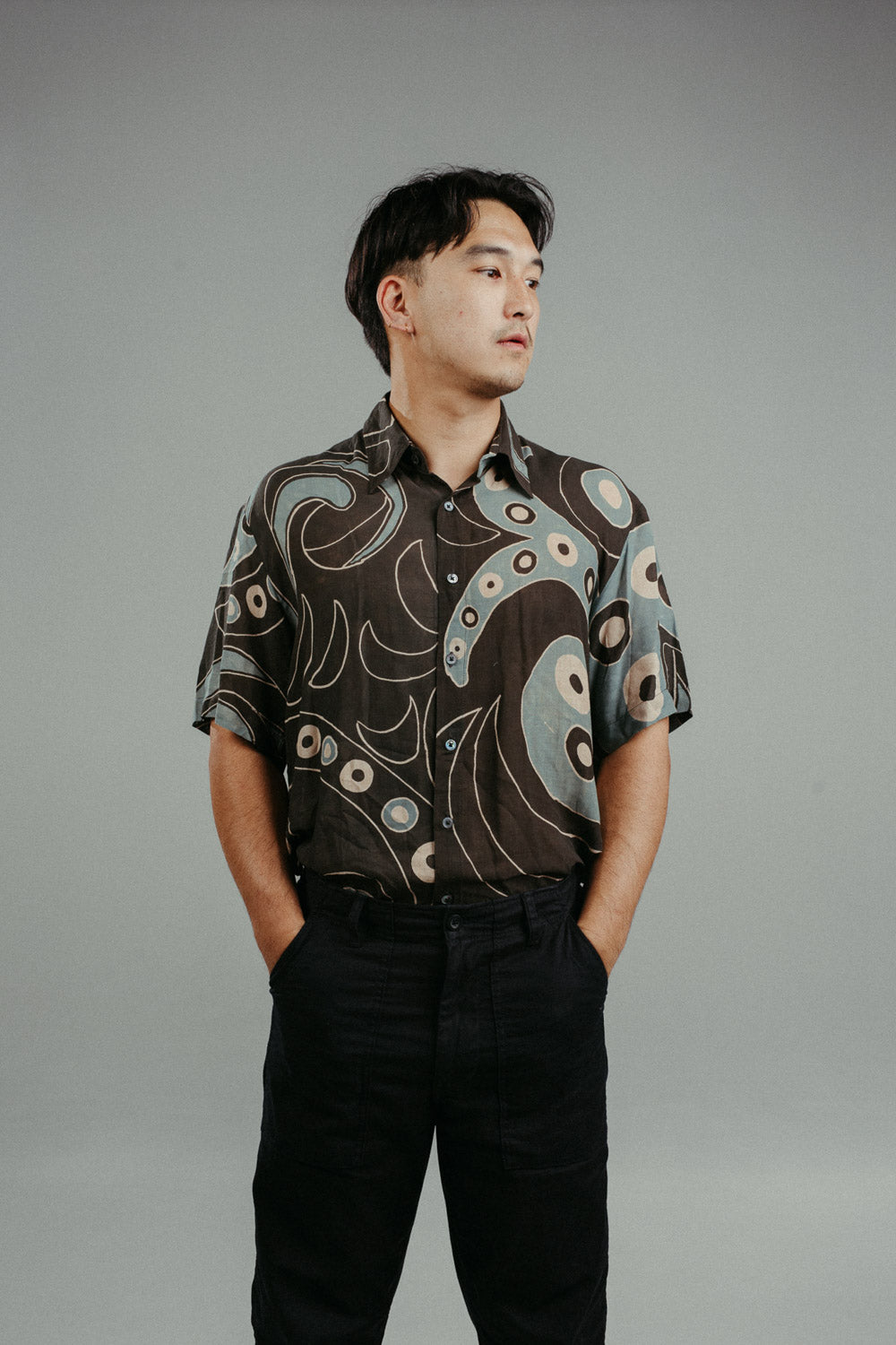 A person wearing a brown handpainted batik shirt with a geometric pattern featuring circles and lines.