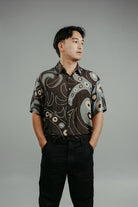 A person wearing a brown handpainted batik shirt with a geometric pattern featuring circles and lines.