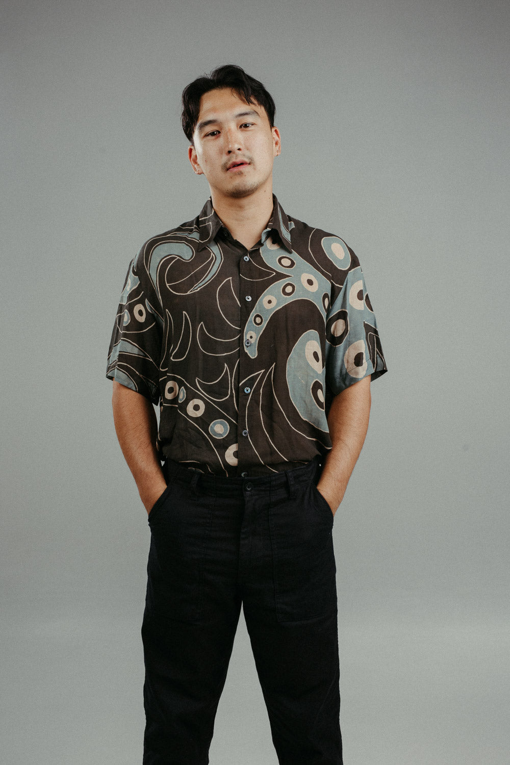 A person wearing a brown handpainted batik shirt with a geometric pattern featuring circles and lines.