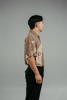 A person wearing a brown handpainted batik shirt with geometric patterns and a classic collar, featuring contrasting recycled seashell marble buttons.