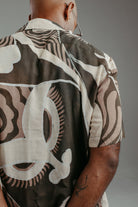 Handpainted Batik cotton shirt worn by a male model in a brown and natural hues featuring pattern of wayang faces.