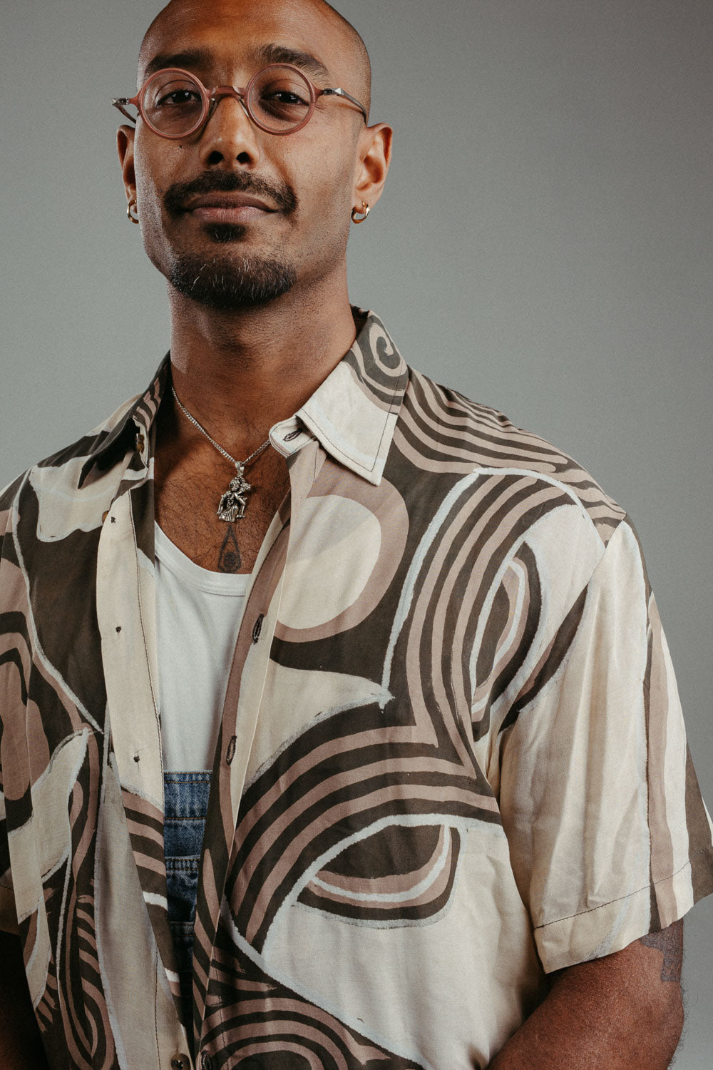 Handpainted Batik cotton shirt worn by a male model in a brown and natural hues featuring pattern of wayang faces.