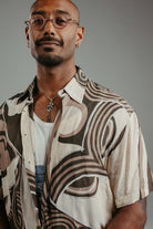 Handpainted Batik cotton shirt worn by a male model in a brown and natural hues featuring pattern of wayang faces.