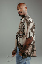 Handpainted Batik cotton shirt worn by a male model in a brown and natural hues featuring pattern of wayang faces.