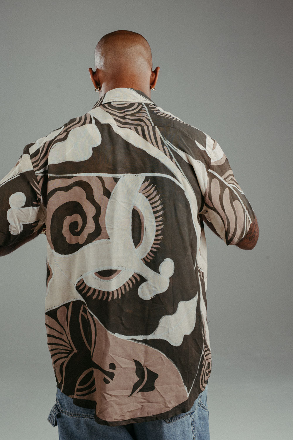 Handpainted Batik cotton shirt worn by a male model in a brown and natural hues featuring pattern of wayang faces.